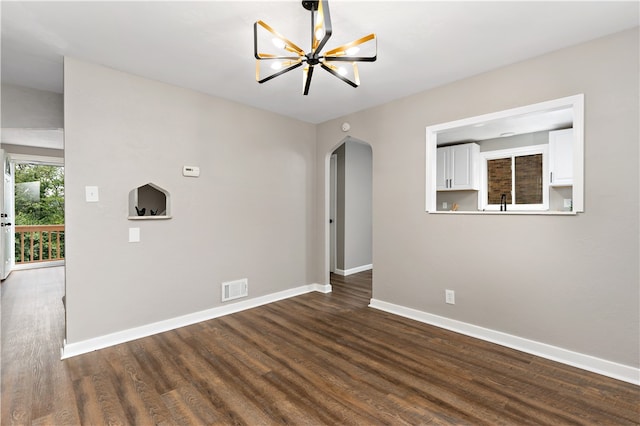 unfurnished room featuring an inviting chandelier and dark hardwood / wood-style flooring