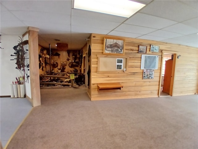 interior space with carpet flooring, wood walls, and a drop ceiling