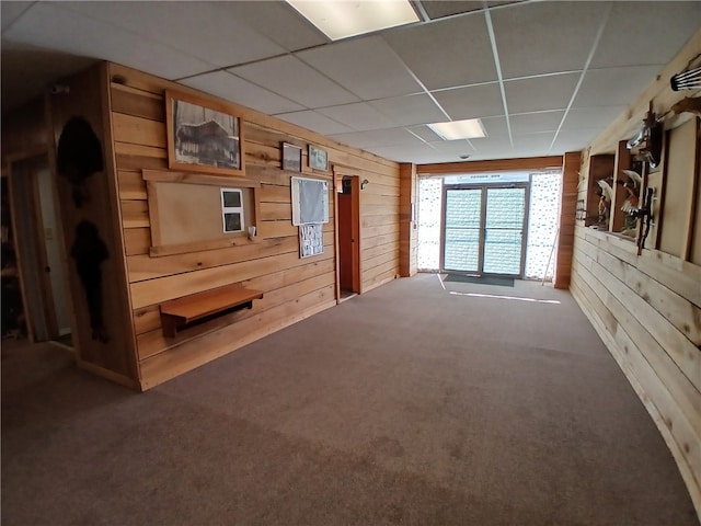 unfurnished room with a drop ceiling, wood walls, and carpet flooring