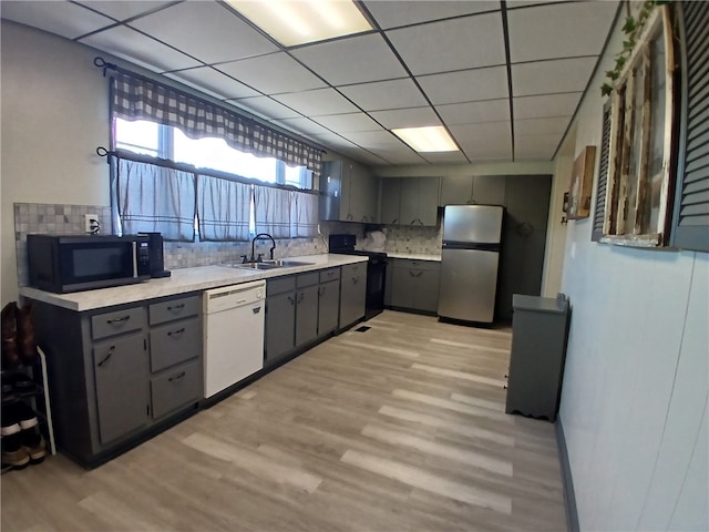 kitchen featuring white dishwasher, light hardwood / wood-style flooring, sink, stainless steel fridge, and decorative backsplash