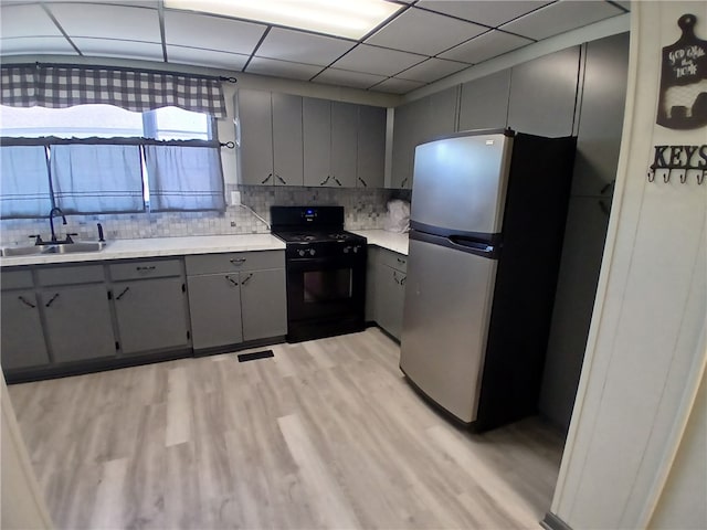 kitchen with black range, light wood-type flooring, sink, stainless steel fridge, and decorative backsplash