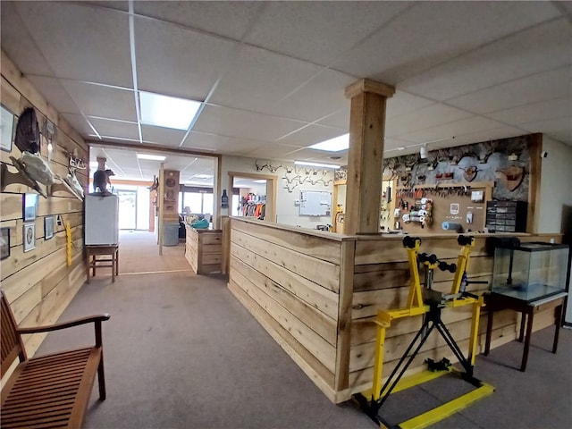 interior space with wood walls, a workshop area, carpet, and a drop ceiling