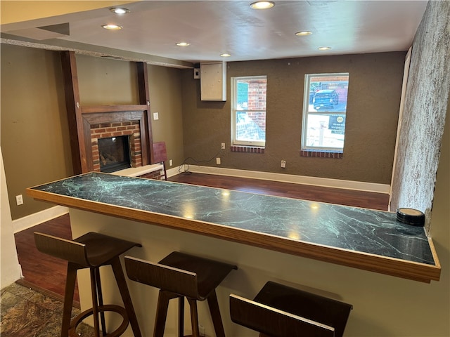 kitchen with a breakfast bar, kitchen peninsula, dark wood-type flooring, and a brick fireplace