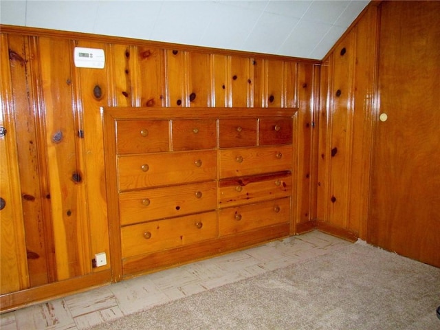 unfurnished room featuring vaulted ceiling, light colored carpet, and wooden walls