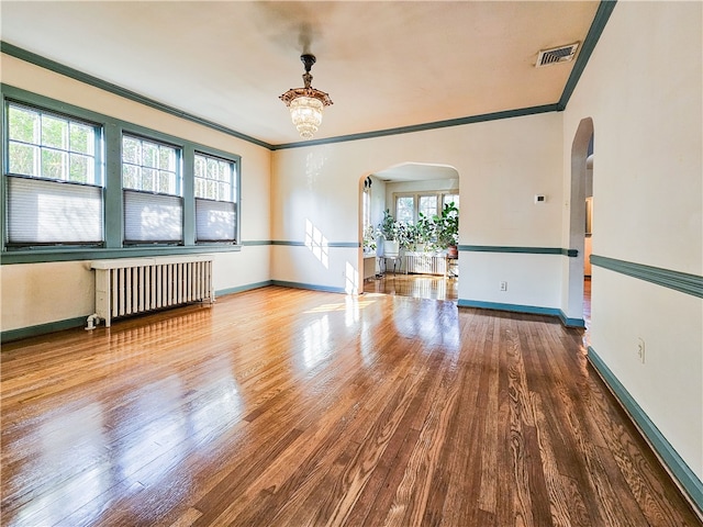 empty room featuring hardwood / wood-style floors, a healthy amount of sunlight, ornamental molding, and radiator