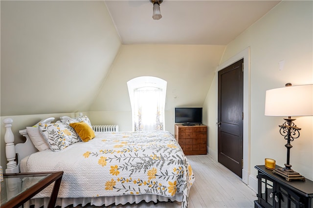 bedroom featuring radiator heating unit, a closet, light wood-type flooring, and vaulted ceiling