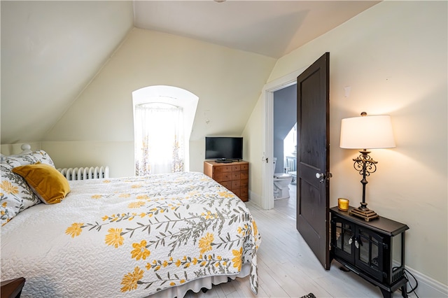 bedroom featuring ensuite bathroom, multiple windows, light wood-type flooring, and lofted ceiling