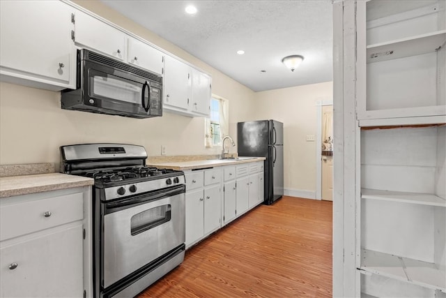 kitchen with sink, a textured ceiling, light hardwood / wood-style flooring, white cabinetry, and black appliances