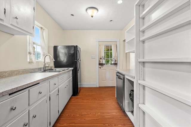 kitchen with light wood-type flooring, stainless steel dishwasher, sink, and black fridge