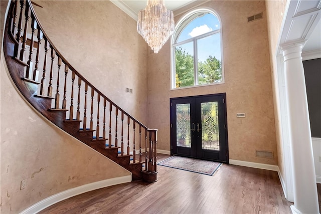 foyer entrance featuring crown molding, hardwood / wood-style floors, french doors, a high ceiling, and an inviting chandelier