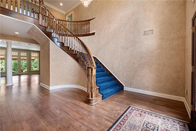 stairs with ornate columns, french doors, hardwood / wood-style flooring, a towering ceiling, and ornamental molding