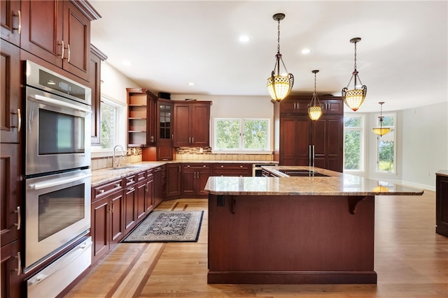 kitchen with pendant lighting, a kitchen bar, stainless steel double oven, and plenty of natural light