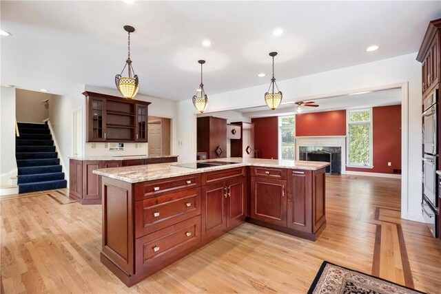 kitchen with light stone countertops, a center island, black electric stovetop, hanging light fixtures, and ceiling fan