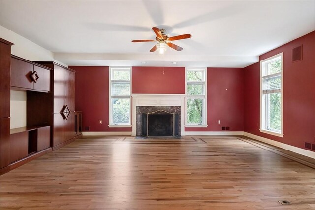 unfurnished living room featuring ceiling fan, a high end fireplace, light hardwood / wood-style flooring, and plenty of natural light