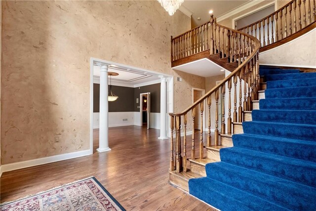 staircase with decorative columns, ornamental molding, and hardwood / wood-style floors