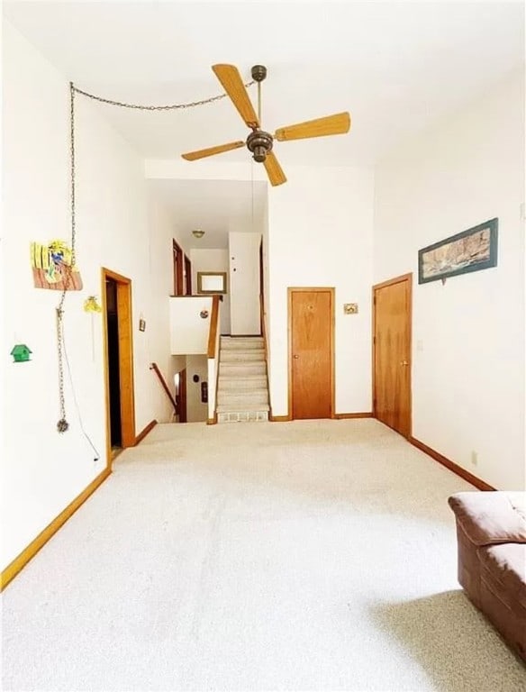 unfurnished living room with ceiling fan, carpet flooring, and a towering ceiling