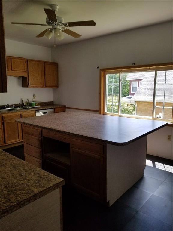 kitchen with a kitchen island, ceiling fan, dark tile patterned flooring, and stainless steel dishwasher