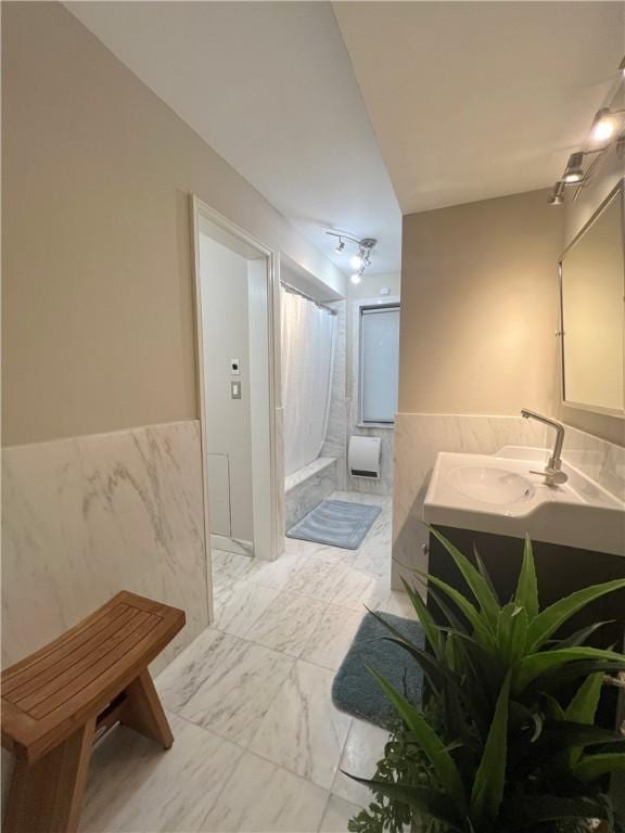 full bathroom featuring double vanity, wainscoting, a sink, marble finish floor, and tile walls