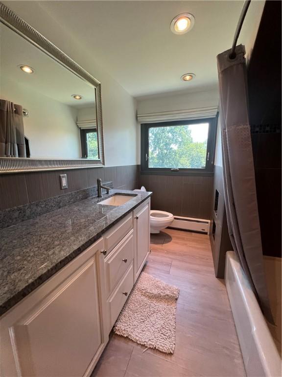 full bathroom featuring wainscoting, toilet, shower / bath combo with shower curtain, vanity, and a baseboard heating unit