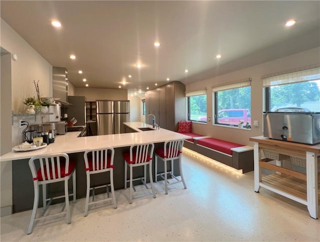 kitchen with light countertops, freestanding refrigerator, a sink, a peninsula, and a kitchen breakfast bar