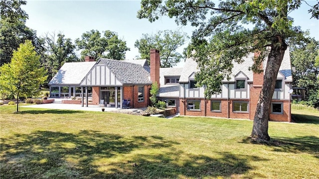 back of property with brick siding, a yard, a chimney, and a patio