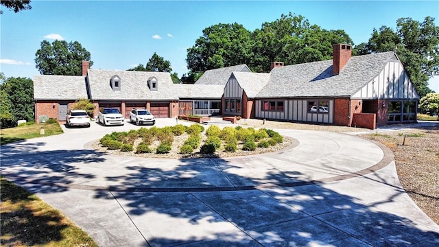 tudor home featuring brick siding, curved driveway, a chimney, and board and batten siding