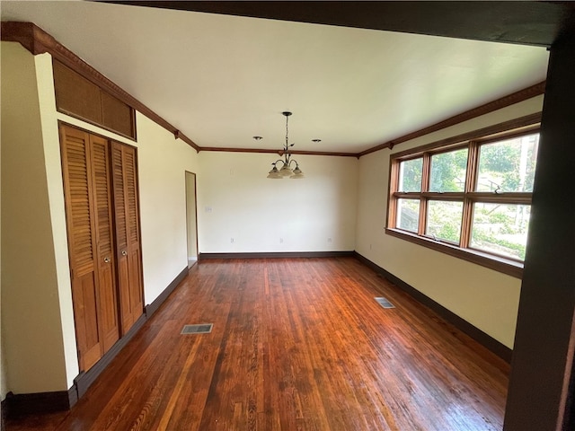 empty room featuring an inviting chandelier, dark hardwood / wood-style flooring, and ornamental molding