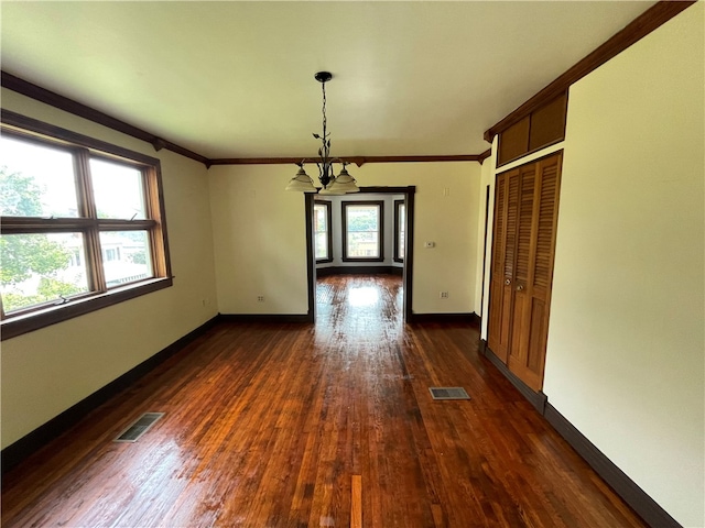 spare room featuring a healthy amount of sunlight, dark hardwood / wood-style flooring, and an inviting chandelier