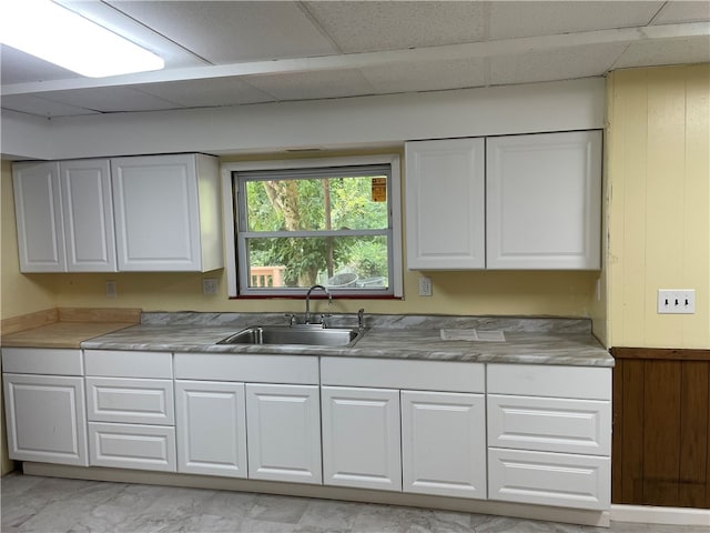 kitchen with sink, a paneled ceiling, white cabinets, and light tile patterned floors