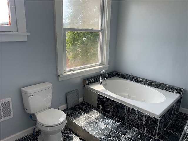 bathroom featuring tiled tub, tile patterned flooring, and toilet