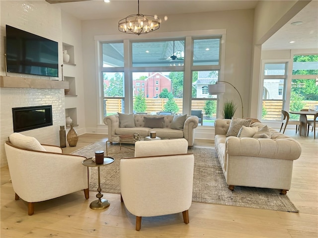 living room with a brick fireplace, a wealth of natural light, a chandelier, and light wood-type flooring