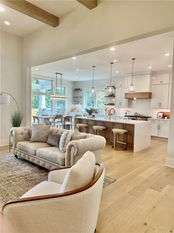 living room with light wood-type flooring, beamed ceiling, a wealth of natural light, and sink