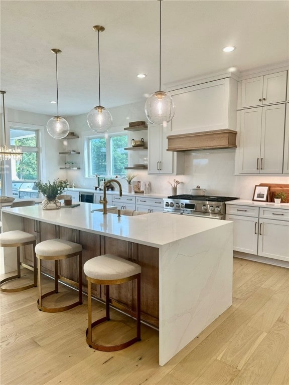 kitchen with white cabinets, stainless steel range, custom range hood, and a large island with sink