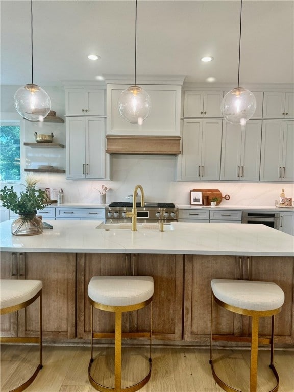 kitchen featuring a kitchen bar, a large island with sink, white cabinetry, and light wood-type flooring