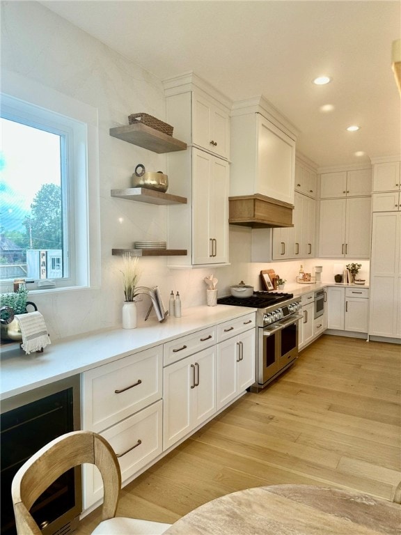 kitchen featuring light hardwood / wood-style floors, premium range hood, white cabinetry, wine cooler, and range with two ovens