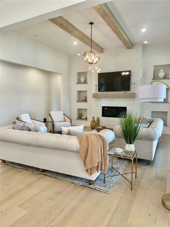 living room featuring built in shelves, beamed ceiling, an inviting chandelier, light hardwood / wood-style floors, and a fireplace