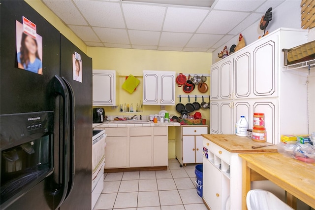 kitchen featuring light tile patterned flooring, a drop ceiling, white electric range, black fridge, and sink