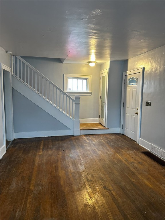 unfurnished living room featuring visible vents, stairway, baseboards, and hardwood / wood-style flooring