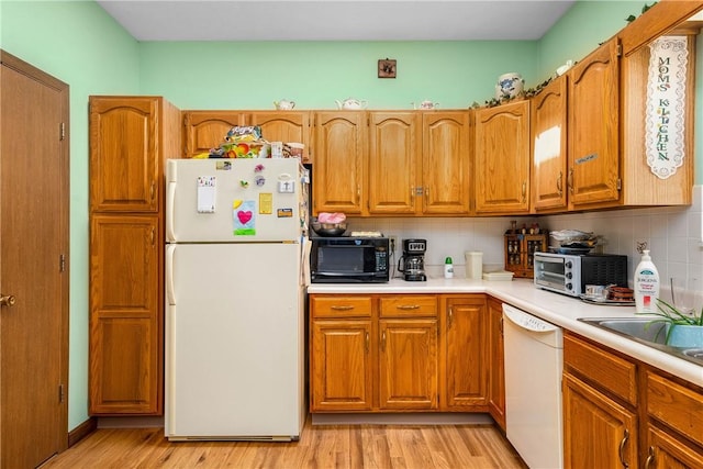 kitchen with tasteful backsplash, white appliances, sink, and light hardwood / wood-style flooring