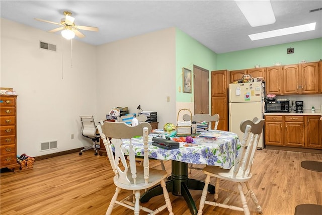 dining room featuring ceiling fan, light hardwood / wood-style floors, and a skylight