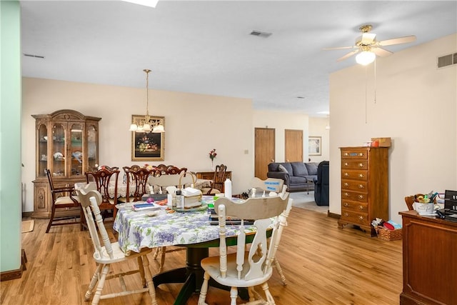 dining space with ceiling fan with notable chandelier and light hardwood / wood-style floors