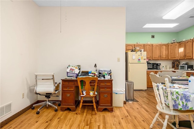 home office featuring a skylight and light hardwood / wood-style flooring