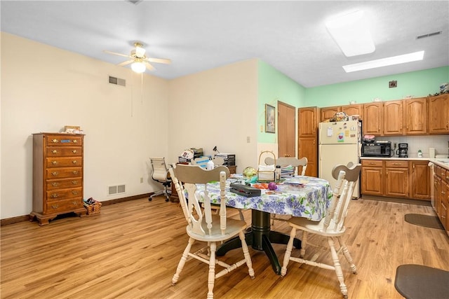 dining area featuring ceiling fan, a skylight, and light hardwood / wood-style floors