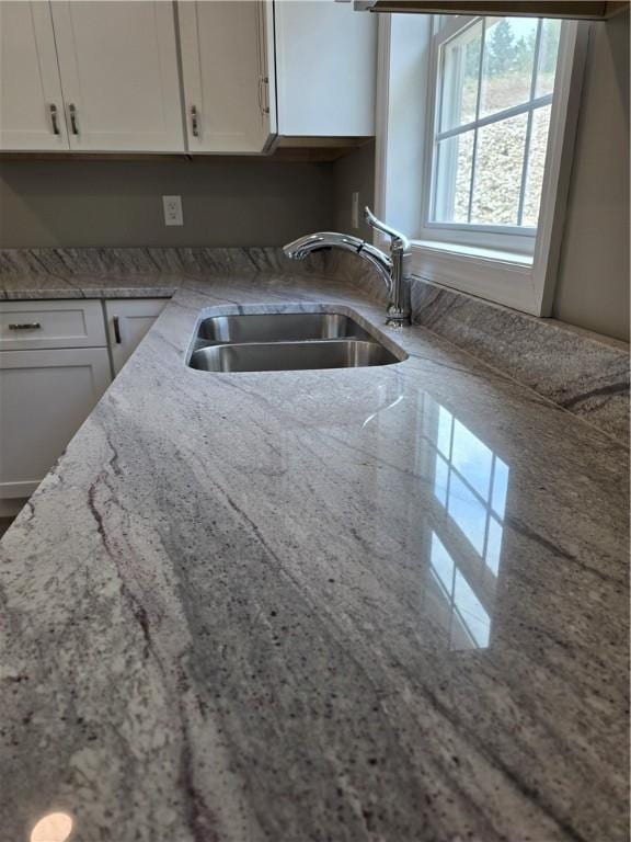 kitchen with white cabinetry, sink, and light stone countertops