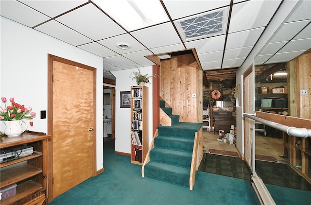 interior space featuring dark colored carpet, a paneled ceiling, and wood walls