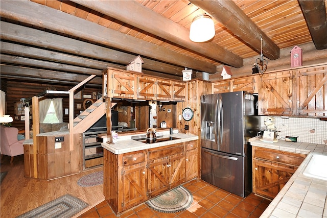 kitchen featuring beam ceiling, decorative backsplash, stainless steel fridge with ice dispenser, light tile patterned floors, and tile counters