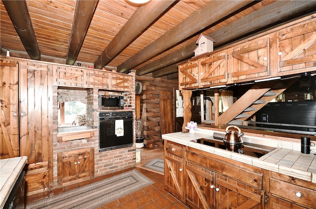 kitchen with beamed ceiling, tile patterned floors, tile counters, rustic walls, and black appliances