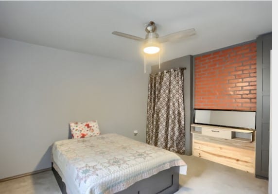 bedroom featuring concrete flooring, ceiling fan, and brick wall