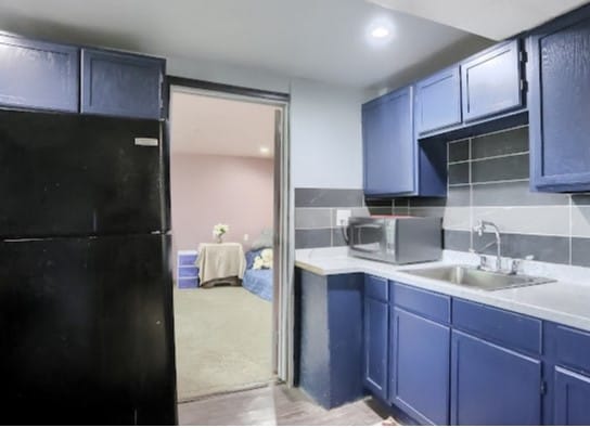 kitchen featuring light carpet, blue cabinetry, black refrigerator, sink, and decorative backsplash