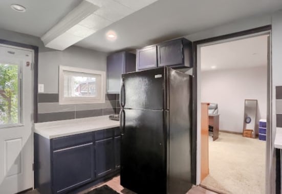 kitchen featuring tasteful backsplash, black refrigerator, light carpet, and blue cabinetry